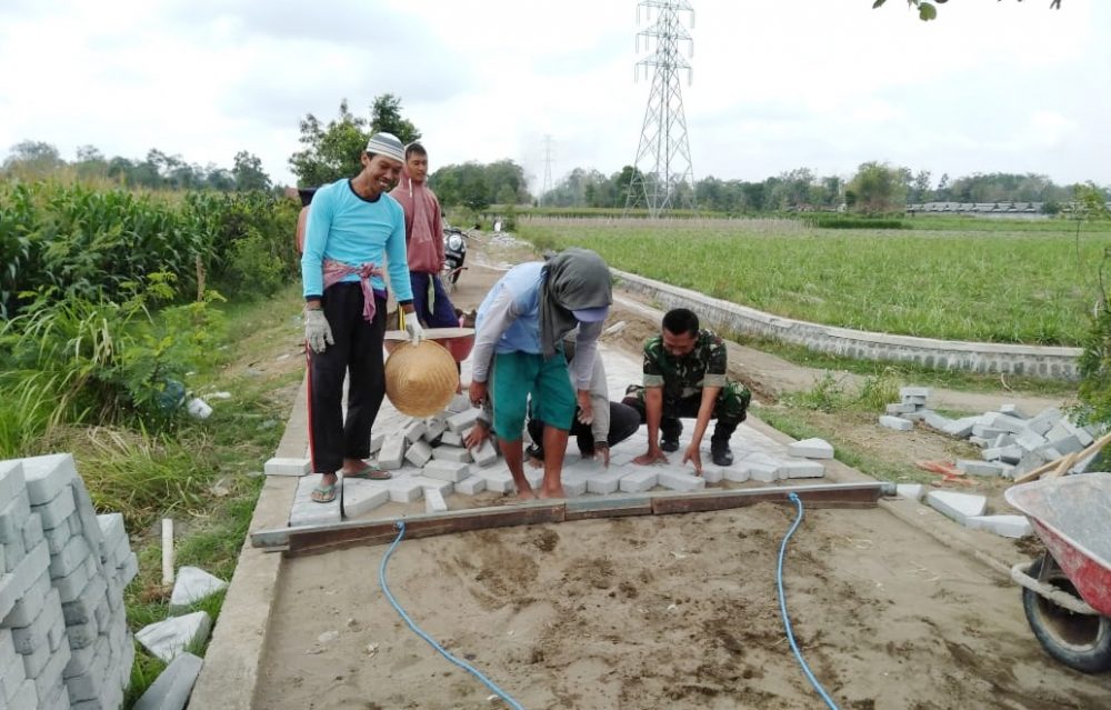 Perbaiki Akses Jalan, Serma Munjali Bantu Warga Memasang Paving Jalan Desa